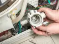 Hände halten eine Waschmaschine-Pumpe, die nicht abpumpt. Kabel und Schläuche sind sichtbar.