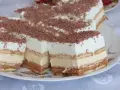 Szybkie ciasto bez pieczenia z budyniem i herbatnikami, przełożone kremem karmelowym, posypane wiórkami czekolady.