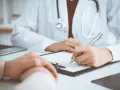 Lekarz wypełnia dokumentację medyczną, pacjent czeka na informację, ile NFZ płaci za wizytę u specjalisty.