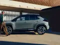 Stylowa kobieta w luźnych spodniach i zielonej kurtce idzie obok swojego nowego, miejskiego auta. Idealne auto dla kobiety, które podkreśla jej indywidualność.