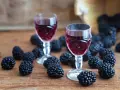 Dwa kieliszki z rubinową nalewką z jerzyn, otoczone świeżymi owocami na drewnianym blacie.