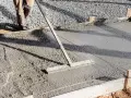 Un ouvrier utilise un râteau pour lisser du béton frais, étape essentielle pour faire une dalle béton solide.