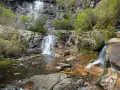 Las chorreras de despeñalagua, cascadas de agua blanca cayendo sobre rocas rojizas y verdes arbustos en un paisaje rocoso.