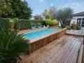 Aménagement abord piscine hors sol en bois, avec terrasse et végétation luxuriante.