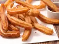 Goldbraune Churros, frisch frittiert, mit Zucker bestreut. Ein Churro wird in eine Schüssel mit Schokoladensauce getunkt. Ein echtes Churros Rezept Original.