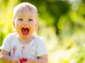 Uśmiechnięte 1.5 roczne dziecko nie mówi mama, ale z radością trzyma truskawkę.
