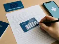 Ręka wypełnia formularz, obok karta EKUZ i paszport. Czas oczekiwania na dokumenty.