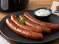 Vier gebratene Merguez-Würste auf einem Teller, serviert mit Dip. Ein Airfryer-Guide-Logo ist im Hintergrund zu sehen. Perfekt für ein schnelles Merguez Rezept.