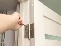 Dłoń dokręca śrubę w zawiasie drzwi, wykonując regulację zawiasów drzwi.