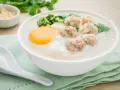 Miseczka pysznego congee z mięsnymi klopsikami, jajkiem i szczypiorkiem. Idealne na rozgrzewający posiłek.