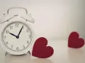 Biały budzik pokazuje 10:08. Obok niego leżą dwa czerwone serca. 0202 znaczenie: czas na miłość.