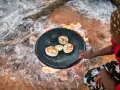 Kobieta piecze chlebki na ogniu, czuć prawdziwy smak Afryki.