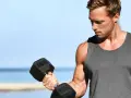 Mężczyzna ćwiczy biceps na plaży, zastanawiając się, ile serii na biceps w tygodniu da najlepsze efekty.