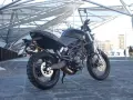 La Moto Morini Scrambler 1200, nera e imponente, si staglia sotto una struttura metallica moderna.
