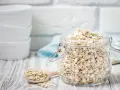 Ein Glas voller haferflocken gemahlen, bereit für ein gesundes Frühstück. Daneben ein Holzlöffel mit weiteren Flocken.