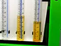 Trzy menzurki z podziałką. W dwóch z nich widać żółty płyn, prawdopodobnie benzyna w oleju, na poziomie około 50 i 40 ml.