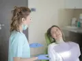 Uśmiechnięta pacjentka na fotelu stomatologicznym słucha dentystki. To obrazek z gabinetu, gdzie odbywają się studia stomatologiczne.