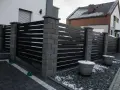 Nowoczesne ogrodzenie z betonowych słupków i ciemnych paneli. Taka wysokość ogrodzenia bez pozwolenia zapewnia prywatność.