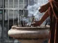Manos monje en túnica marrón colocando varillas de incienso en un cuenco de piedra, creando humo para limpiar el ambiente.