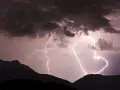 Gewitter in den Bergen: Blitze zucken durch dunkle Wolken über silhouettierten Gipfeln. Ein dramatisches Naturschauspiel.