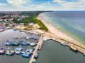 Port rybacki we Władysławowie, województwo pomorskie, tętni życiem. W tle rozciąga się plaża pełna turystów i morze.