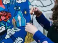 Une artiste, dans son métier artistique, trempe son pinceau dans l'encre pour peindre une toile aux motifs surréalistes : une fleur, un œil, des silhouettes.