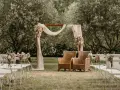 Un décor champêtre pour une célébration laïque : chaises blanches, arche fleurie, fauteuils en rotin sous les oliviers.
