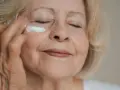 Eine Frau über 70 trägt eine feuchtigkeitsspendende Creme auf. Ihre Augen sind geschlossen, während sie sich um ihre Haut kümmert.