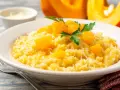 Un cremoso risotto de calabaza, adornado con trozos de calabaza y perejil fresco, espolvoreado con queso rallado.