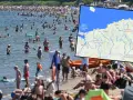 Tłum ludzi na plaży i w wodzie. Mapa pokazuje polskie wybrzeże Bałtyku, gdzie letnie temperatury są idealne do kąpieli.