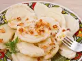 Pyszne pierogi ruskie z farszem Magdy Gessler, posypane skwarkami. Na talerzu z tradycyjnym wzorem.
