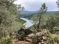 Vista panorámica del embalse de El Vado, rodeado de pinos y montañas. El agua serena refleja el cielo nublado.