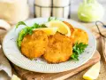 Knusprige Kohlrabi-Schnitzel auf einem Teller mit Erbsenpüree, Zitrone und Petersilie. Ein köstliches vegetarisches Gericht.