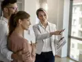 Kobieta w jasnej marynarce pokazuje coś na planach młodym ludziom.