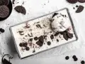 Cremiges Oreo Eis in einer Metallform, garniert mit ganzen und zerbrochenen Keksen. Ein Löffel Eis liegt obenauf.