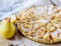 Délicieuse tarte aux poires, saupoudrée de sucre glace, avec des amandes et des poires fraîches à côté.