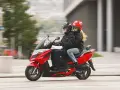 Para jadąca na czerwonym skuterze 125, ubrana w kurtki i kaski, cieszy się jazdą.