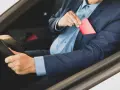 Mężczyzna w garniturze wkłada czerwoną kartkę, przypominającą rejestracje dyplomatyczne, do kieszeni marynarki.