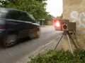 Ein Blitzer, der gerade ein Auto fotografiert, wie sehen Blitzer ohne Blitz aus? Dieses Gerät steht am Straßenrand, bereit für Geschwindigkeitsünder.