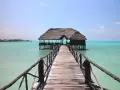 Drewniany pomost prowadzi do chatki na palach na turkusowej wodzie. Idealne miejsce na wiza zanzibar.