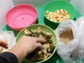 Mani che mescolano cibo per galline in una ciotola verde, con ingredienti come crusca, verdure e mele a cubetti.