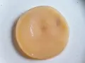 Disque de kombucha moisi, d'une couleur beige pâle, posé sur une assiette blanche.