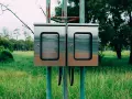 Dwa metalowe słupki z zamontowanymi skrzynkami, przygotowane do podłączenia prądu do działki bez domu.