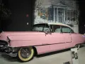 Ein rosafarbener Cadillac, der einst Elvis Presley gehörte, steht vor einer gemalten Kulisse von Graceland.