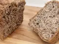 Chleb z siemienia lnianego, pokrojony na desce. Widoczny bochenek i dwa kromki, pełne ziaren.