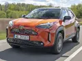 Pomarańczowa Toyota Yaris Hybrid GR Sport pędzi po drodze, otoczona zielenią.