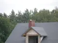 Ceglany komin systemowy na dachu pokrytym papą. W tle las.