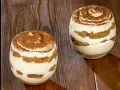 Due bicchieri di tiramisù senza uova, stratificati con crema e savoiardi, spolverati di cacao su un tavolo di legno.