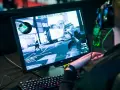 Gracz w słuchawkach gra w CS:GO, próbując jak zmniejszyć ping. Na ekranie widać akcję z gry i klawiaturę.