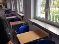 Rzędy pustych ławek i krzeseł w sali lekcyjnej. Za kratami okien widać zieleń. To może być sala egzaminacyjna w więzieniu na Białołęce.